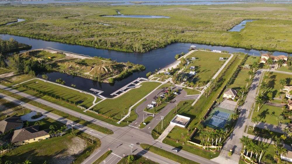 Aerial view of Tropicana Park showing the parking lot, boat docks, a fenced sport court, picnic shelters, walking paths and the beach along a wide waterway, with mangrove preserve behind it.